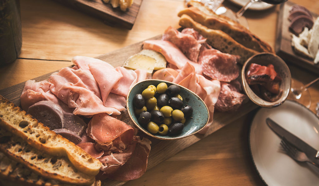 Nahaufname einer Apéroplatte mit Fleischsorten, Brot und Oliven